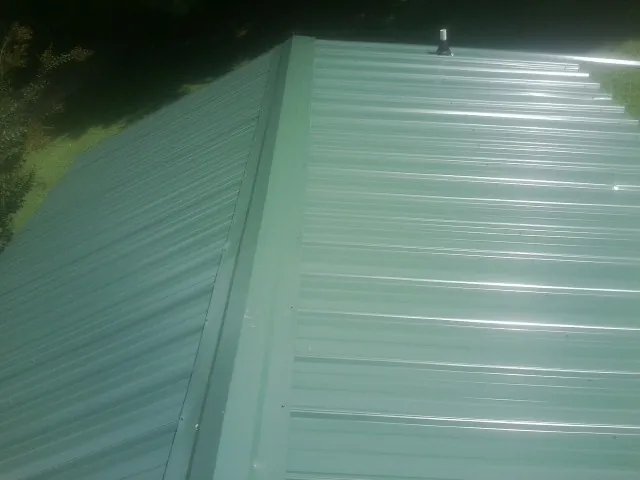New green metal panels meeting at the ridge of a roof — Flat Roof Repair work by our crew in Scranton